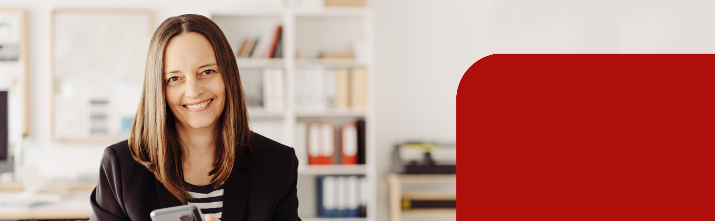 Eine brünette Frau in einem Büro-Setting lächelt in die Kamera