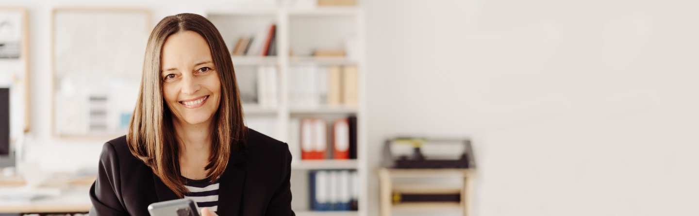 Eine brünette Frau in einem Büro-Setting lächelt in die Kamera